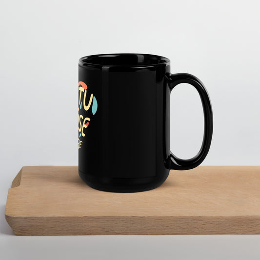 Black mug with colorful "Ubuntu I am because you are" design on a wooden block against a light gray background. side view